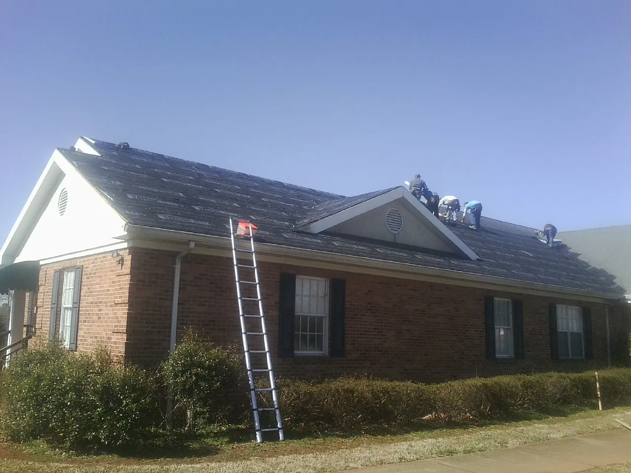 Crew tearing shingles off a brick ranch roof with a ladder set — Metal Roof Repair work by our crew in Durant