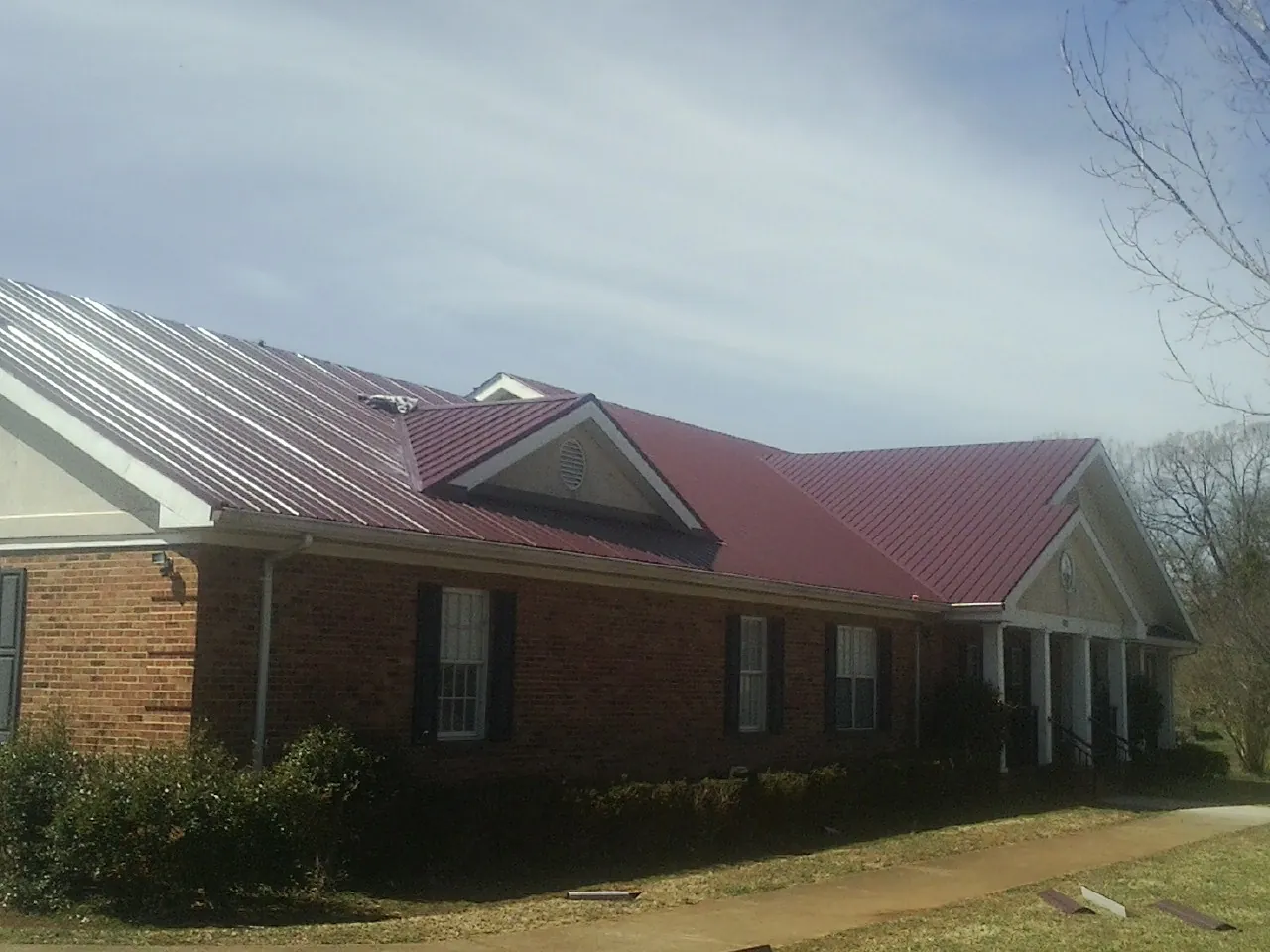 Red metal roof with gabled entries on a long brick building, from a Hail Damage Roof Repair job in Durant
